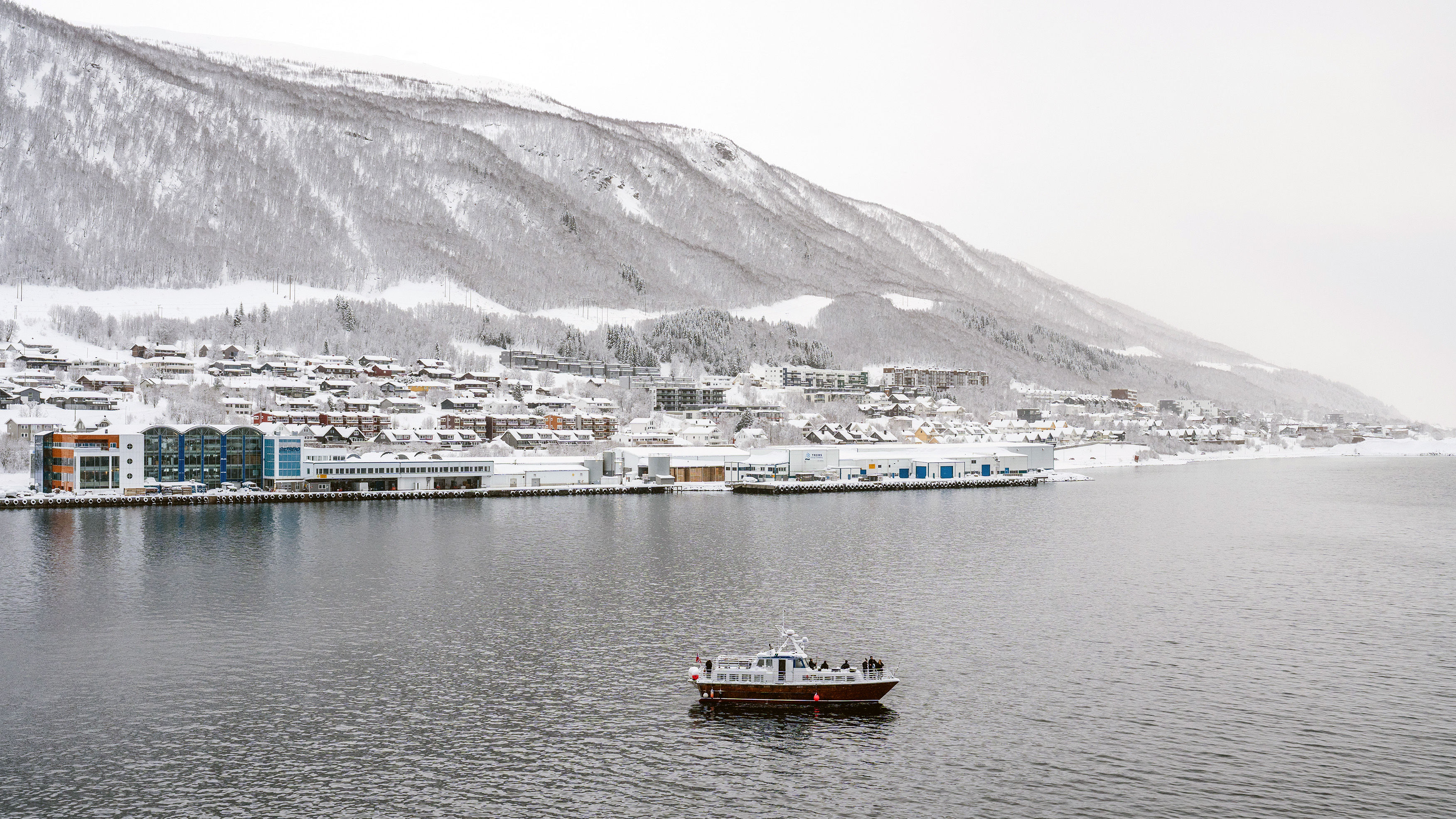 Small boat on a winter fjord beside snow covered Tromso in Norway