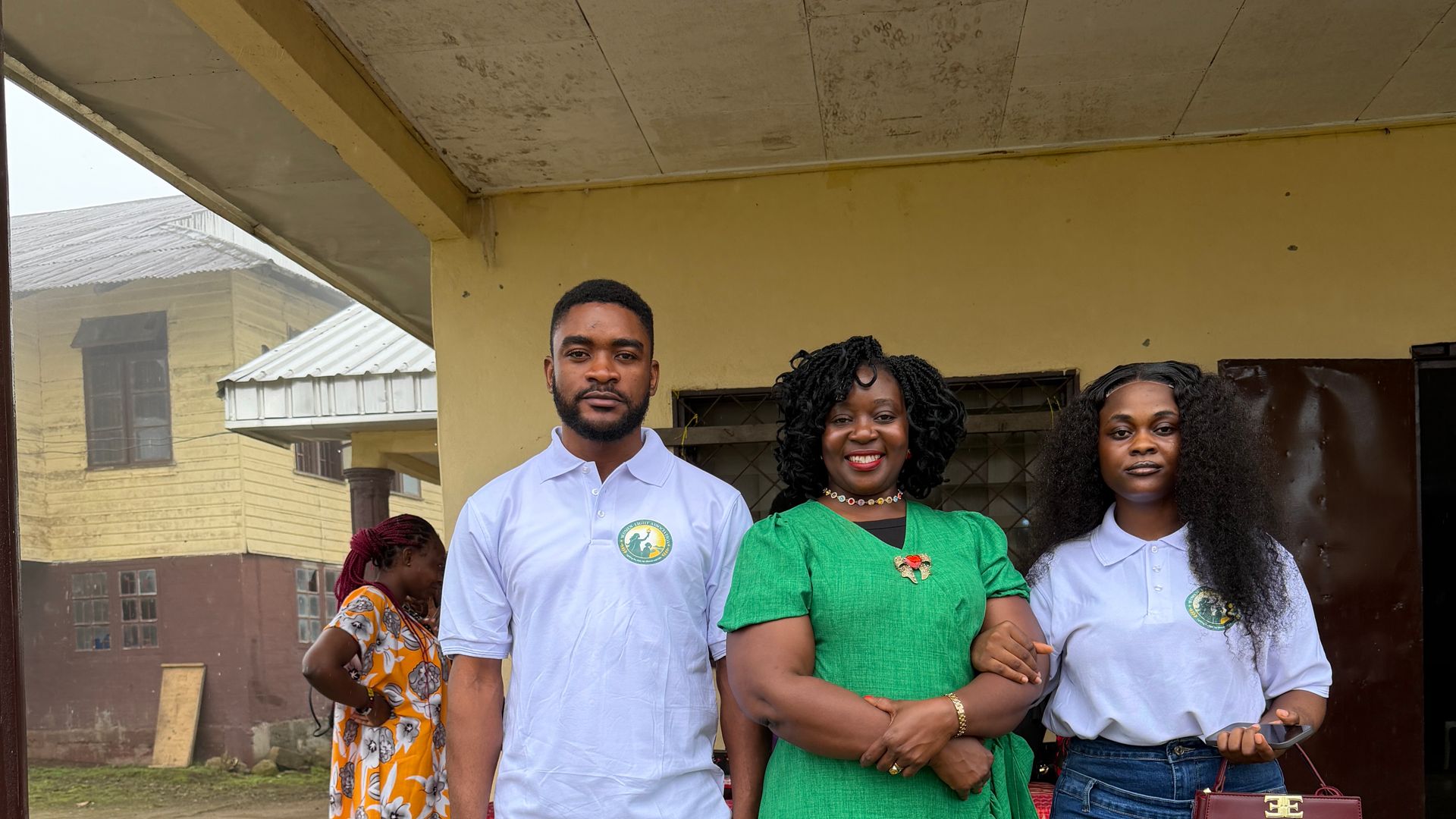 Three members of the Foundation team, two in its logo polo shirts, outside a school building