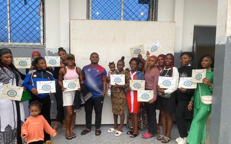 A group of young people hold up certificates outside a building