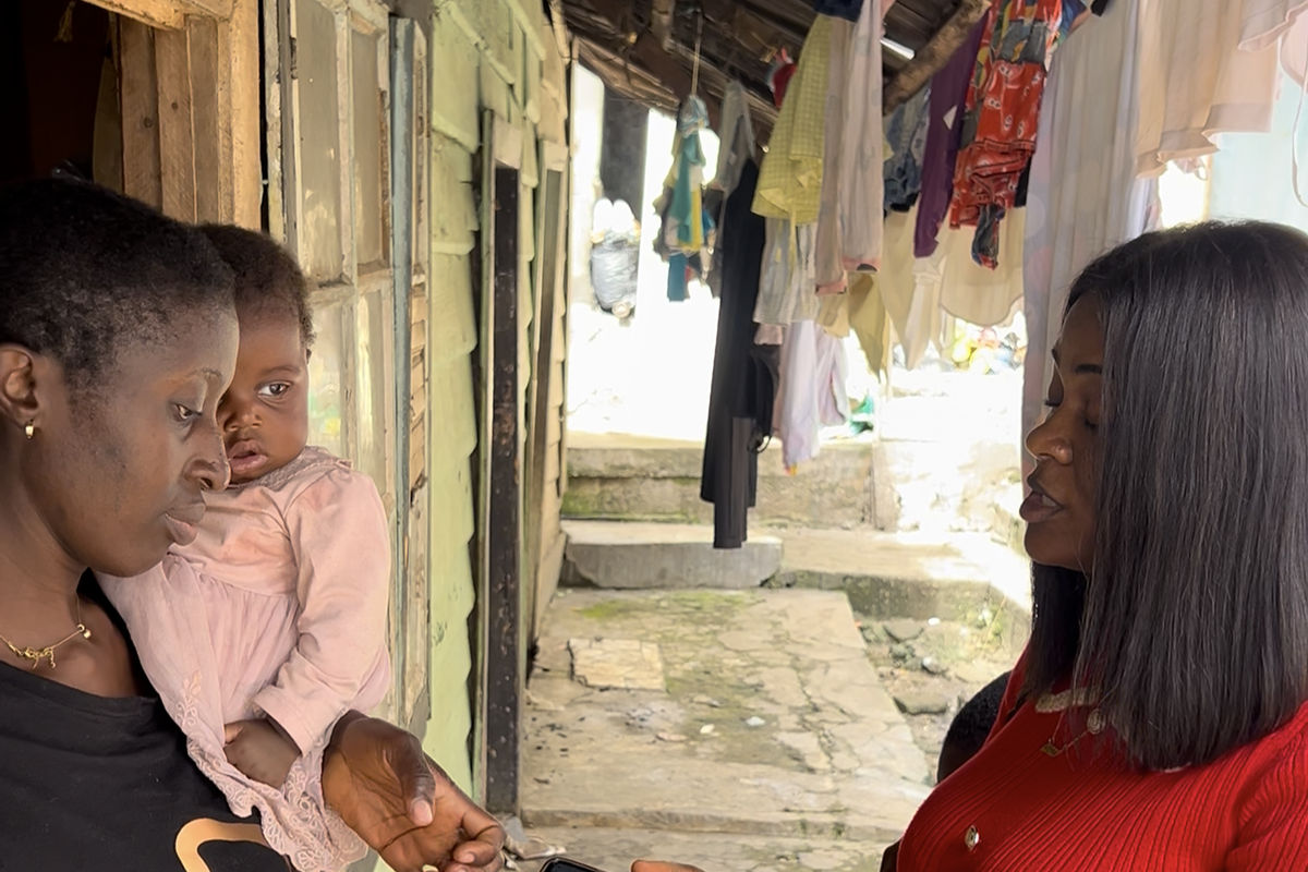 A woman in red talks with a mother holding her baby outside a row of homes
