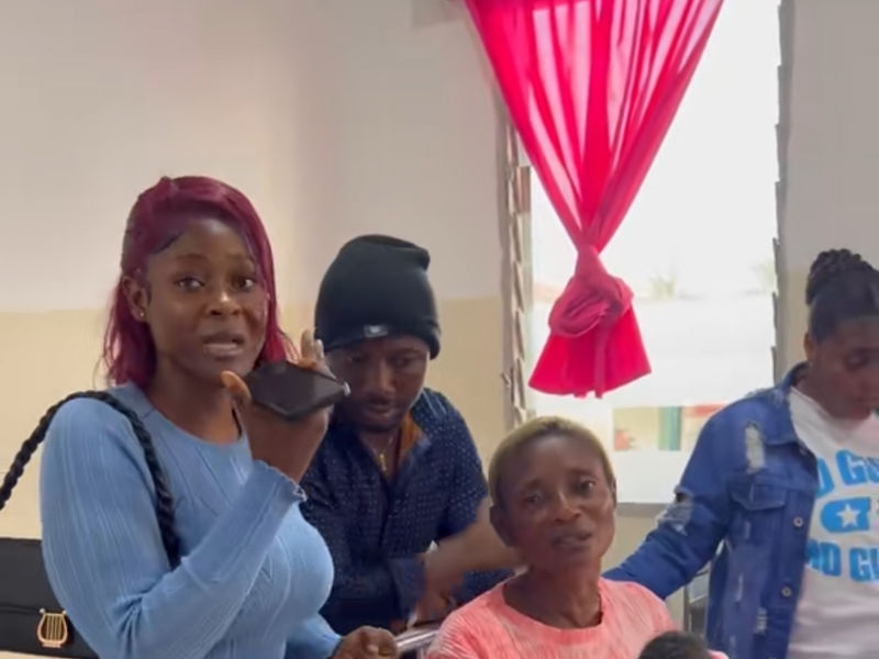A woman speaks into a phone in a room with several other people