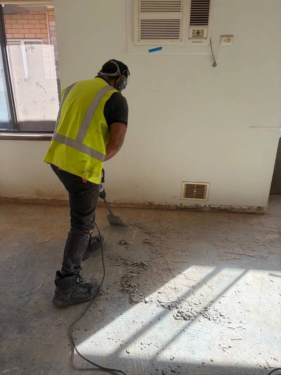 Worker scraping the remains of an old floor off a concrete slab in a Perth home