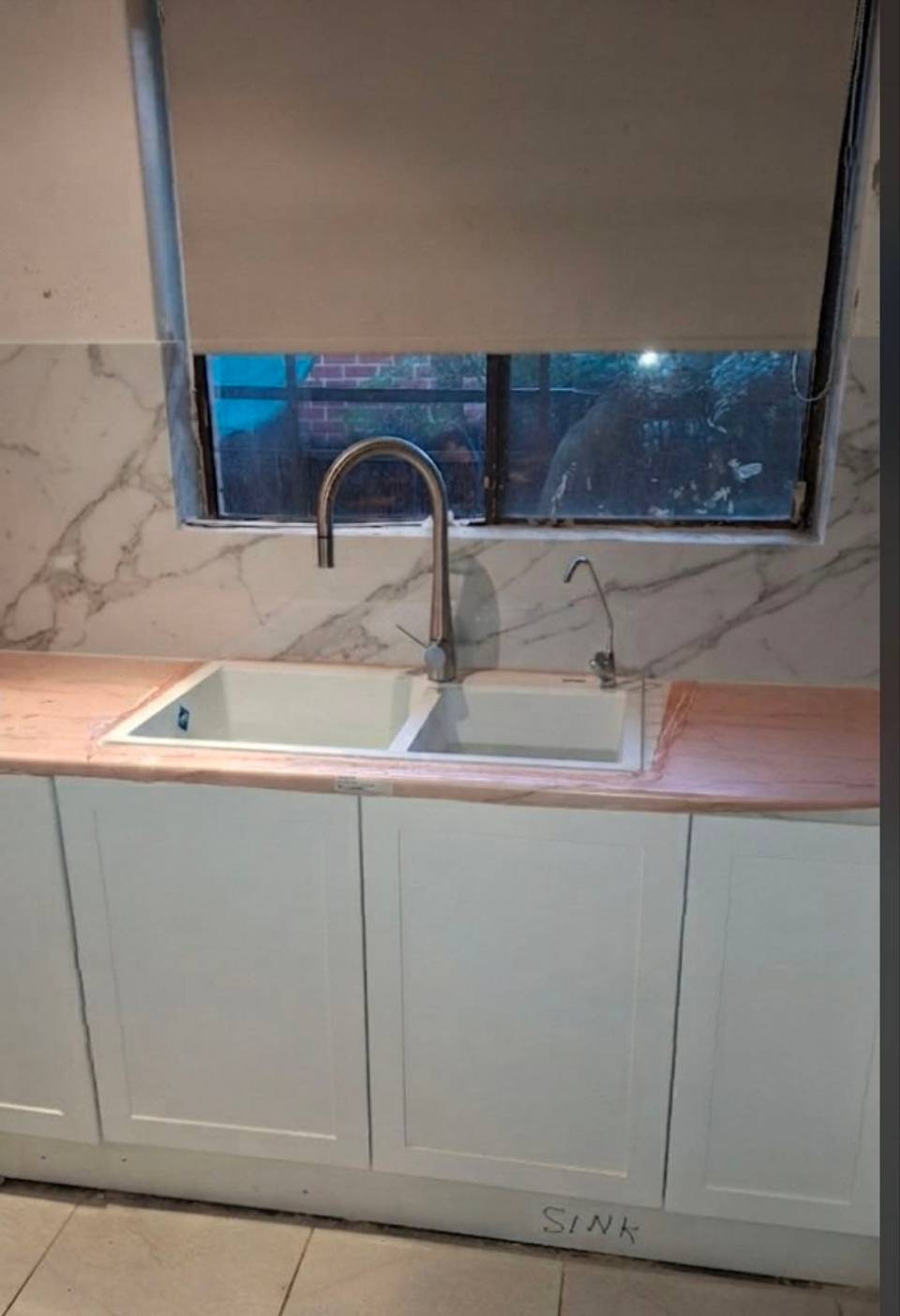 The same Perth kitchen after renovation, with new cabinets and a marble-look splashback under the same window