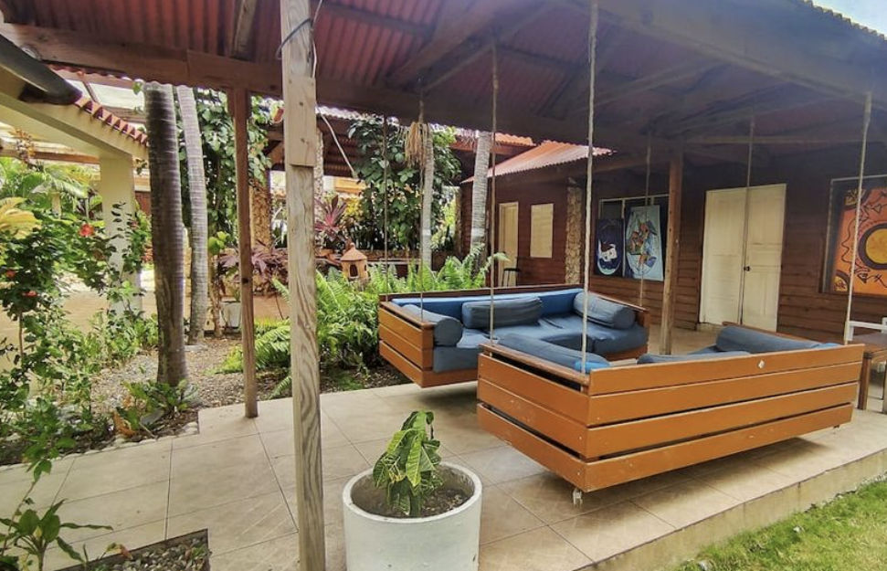 Gran piscina al aire libre en un resort, rodeada de palmeras y un edificio blanco de tres pisos con balcones
