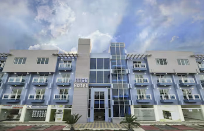 Exterior facade of RD68 Hotel in Punta Cana, featuring a modern three-story building in light blue and white tones with balconies and a large central glass window under a cloudy sky.