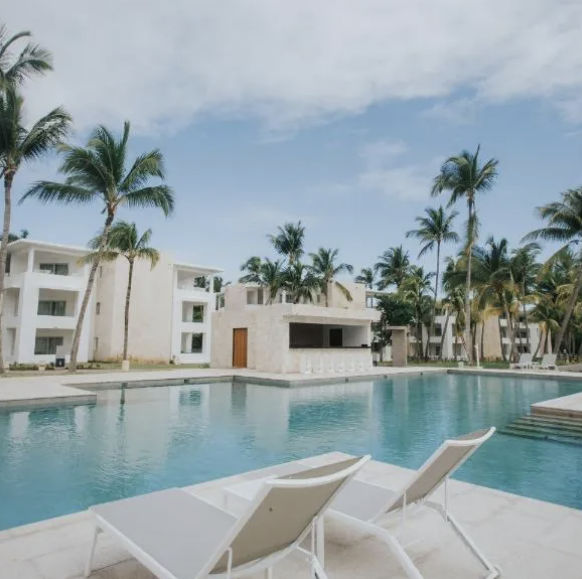 An elevated view of a three-story apartment complex with a swimming pool and tropical garden in Punta Cana