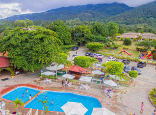 Instalaciones del Jarabacoa River Club iluminadas de noche, con terraza de madera, piscina y vista al río Yaque del Norte rodeado de montañas