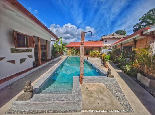 Piscina exterior iluminada del Bali Style Boutique Hotel en Punta Cana rodeada de vegetación tropical y camastros al atardecer