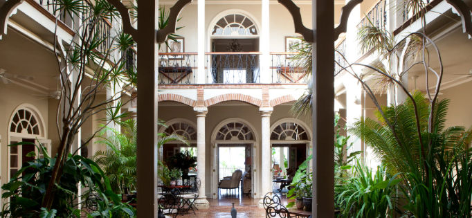 Fachada de estilo colonial de The Peninsula House en Las Terrenas, rodeada de un extenso jardín verde y altas palmeras bajo un cielo despejado