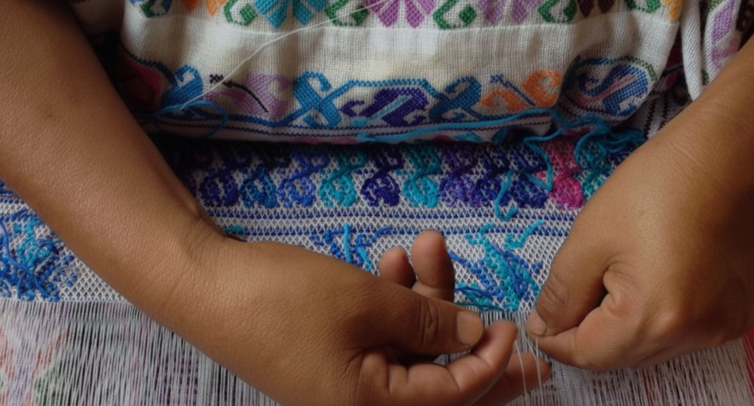 Manos de una artesana bordando un huipil tradicional con hilos de colores vibrantes en Bokobá.