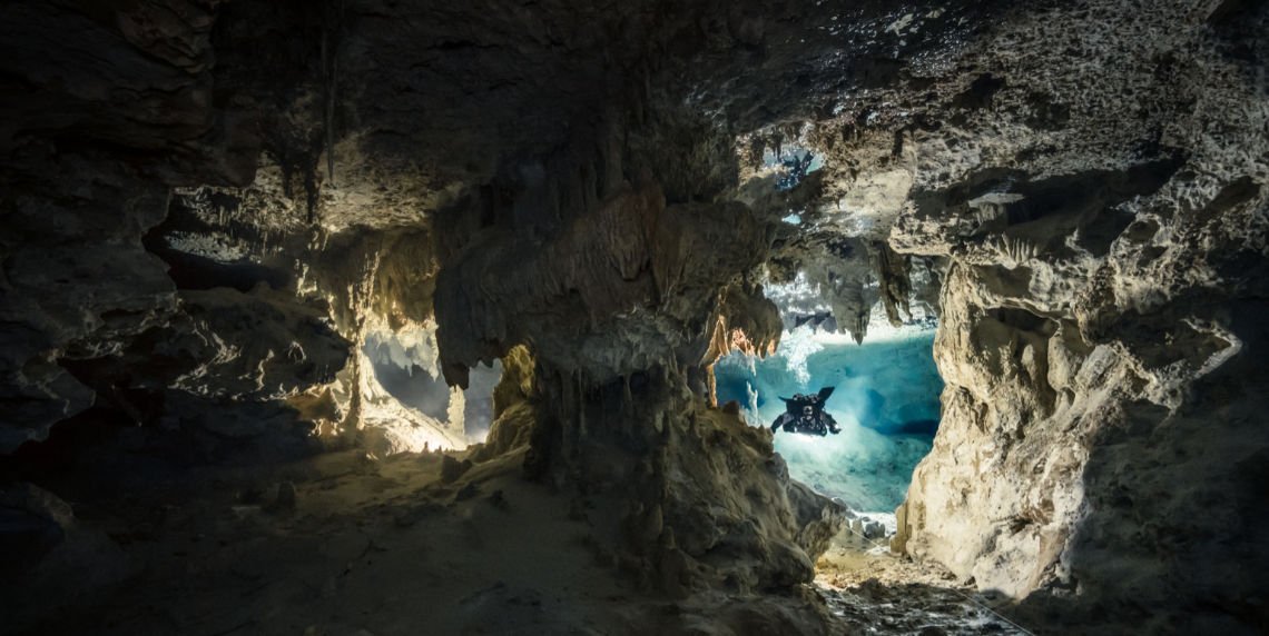 Fotografía del Cenote Chan Hol con buceadores explorando sus aguas cristalinas y estalactitas.
