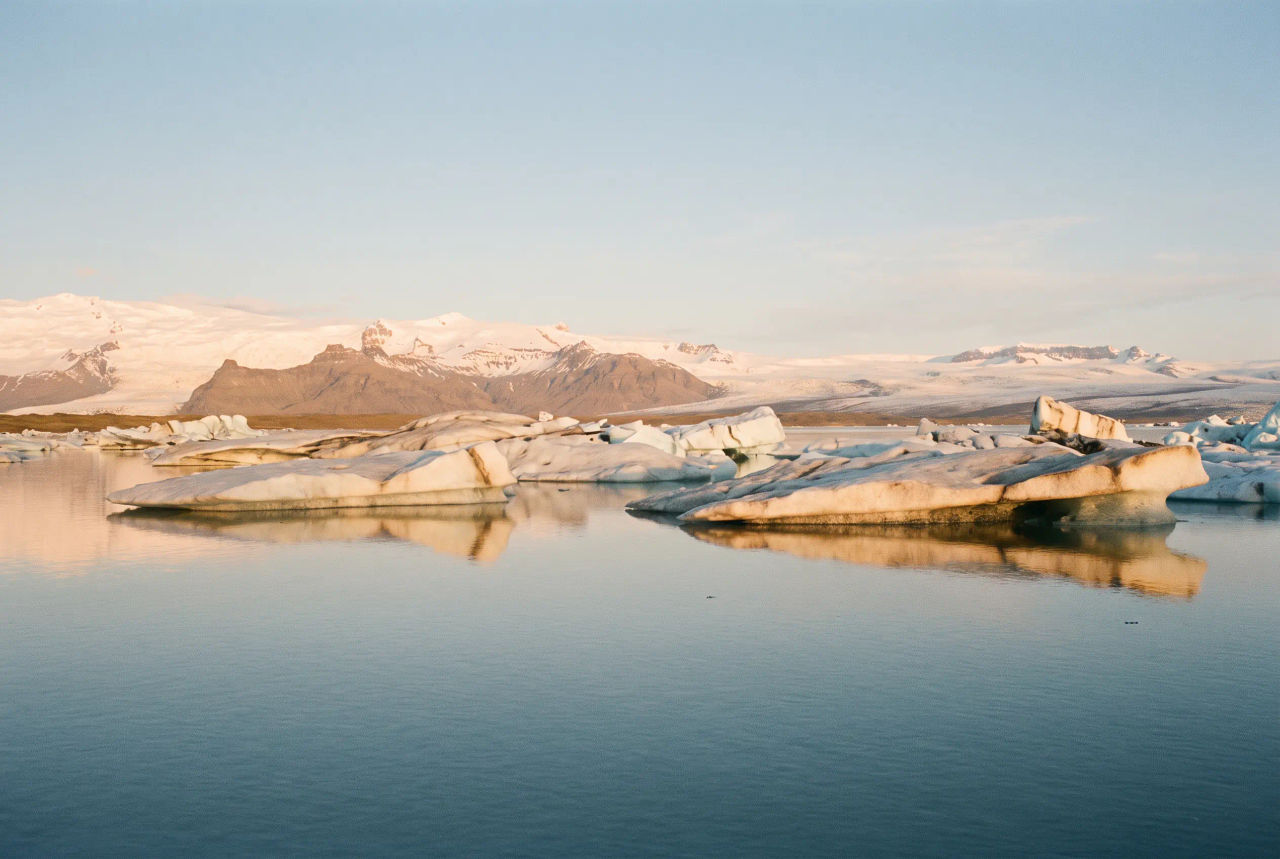 Pale icebergs in a calm lagoon, with snowy mountains in warm late light