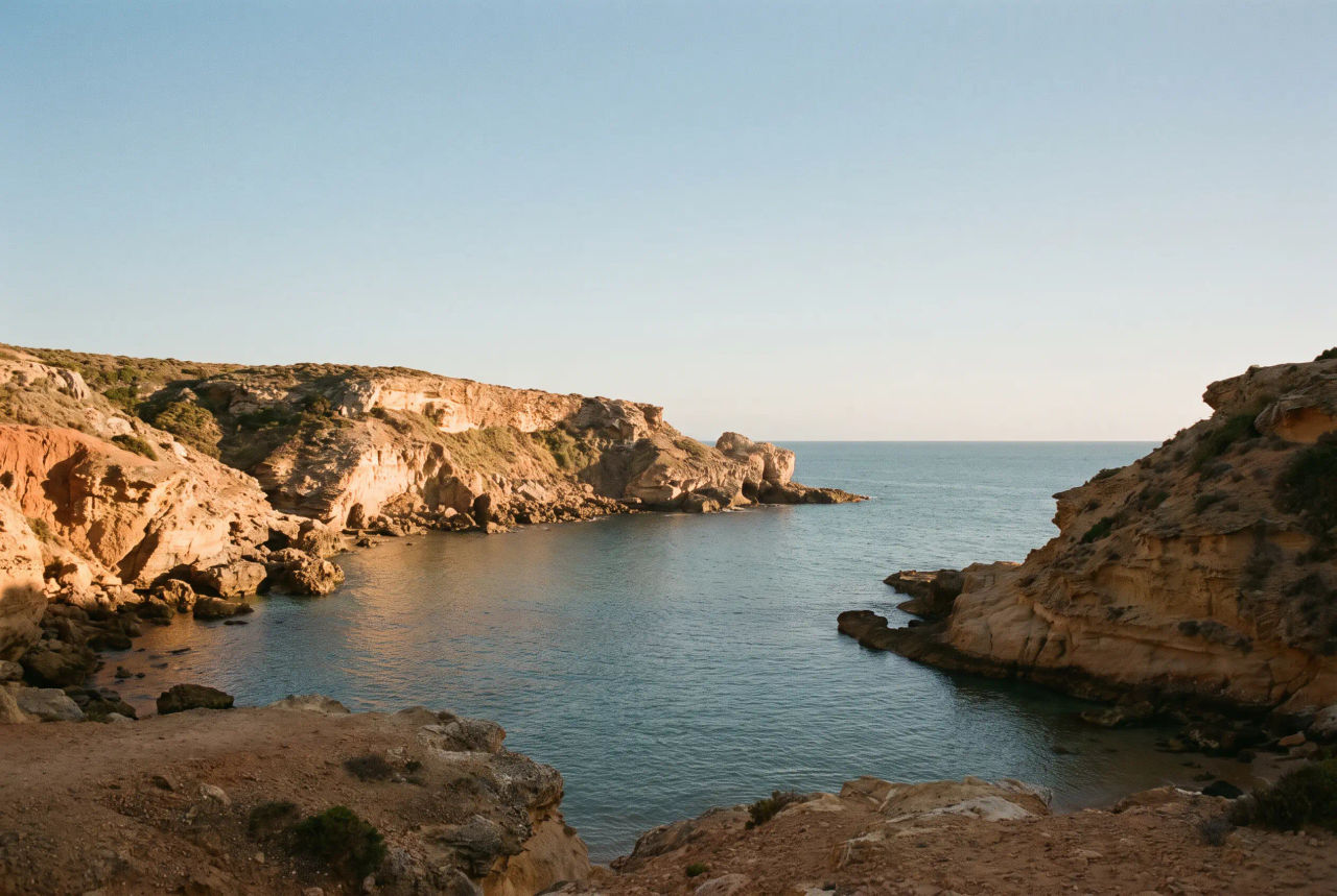 Rocky cove with warm sandstone cliffs and a calm dusty-blue sea
