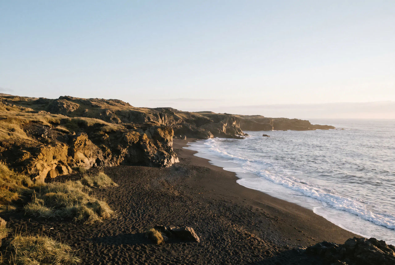 Black-sand volcanic coast with low cliffs and foaming surf in warm late-afternoon light