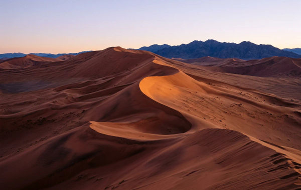 AI-generated terracotta dunes with sweeping wind-shaped ridges and distant blue mountains