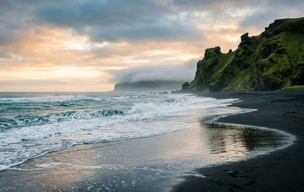 AI-generated black-sand coast with foaming surf, green volcanic cliffs and a warm horizon