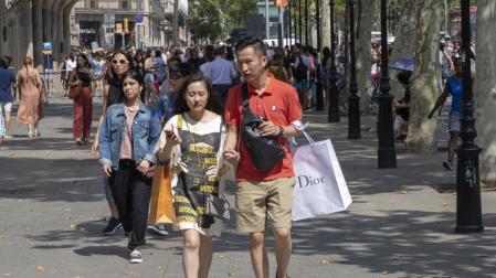 Una pareja pasea por el Passeig de Gracia de Barcelona con bolsas de compra de marcas de lujo