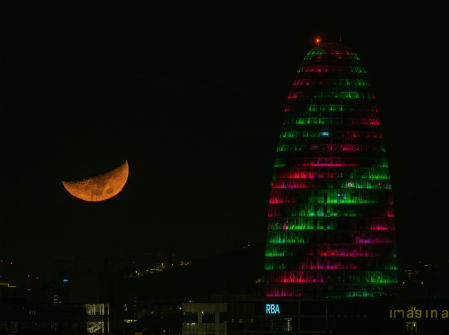 La luna creciente brilla junto a la Torre Glòries iluminada.