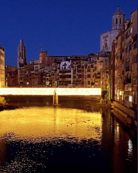 El puente brilla en Girona con la iluminación navideña y los reflejos en el río.