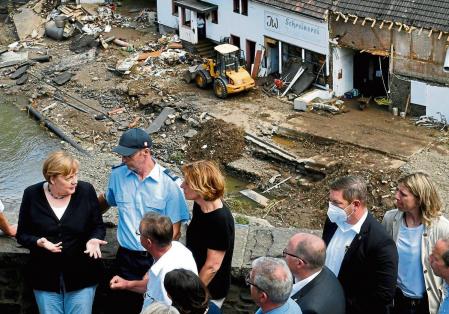 German Chancellor Angela Merkel, left, and the Governor of the German state of Rhineland-Palatinate, Malu Dreyer, rear third left, are seen on a bridge in Schuld, western Germany, Sunday, July 18, 2021 during their visit in the flood-ravaged areas to survey the damage and meet survivors. After days of extreme downpours causing devastating floods in Germany and other parts of western Europe the death toll has risen. (Christof Stache/Pool Photo via AP)