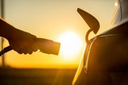 Close up of hand plugging electric charger to socket in electric car at sunrise