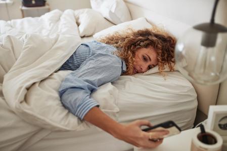 Una mujer mira la hora en el móvil desde la cama