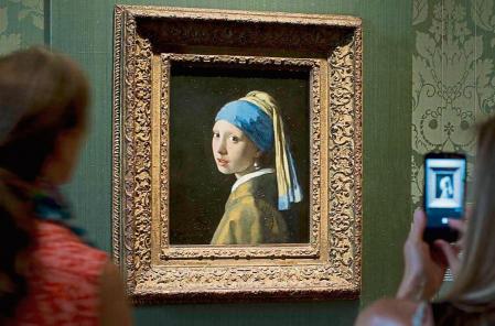 FILE- Visitors take pictures of Johannes Vermeer's Girl with a Pearl Earring (approx. 1665) during a preview for the press of the renovated Mauritshuis in The Hague, Netherlands, June 20, 2014. The Vermeer masterpiece “Girl with a Pearl Earring” has become the latest artwork targetted by climate activists in a protest at the Mauritshuis museum in The Hague on Thursday, Oct. 27, 2022. The museum did not immediately return calls and emails for comment after a video of the protest was posted on Twitter. (AP Photo/Peter Dejong, file)