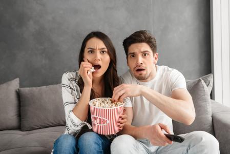 Una pareja ve una película en el sofá de casa con un bol de palomitas de maiz