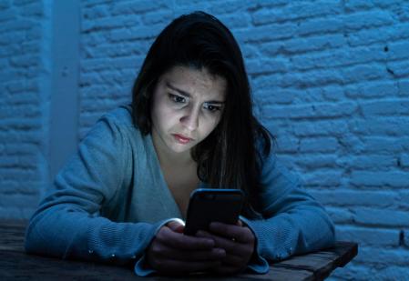 Dramatic portrait of sad scared young woman on smart mobile phone suffering cyber bullying and harassment. feeling lonely, depressed and in fear being online abused by stalker. In dangers of internet.