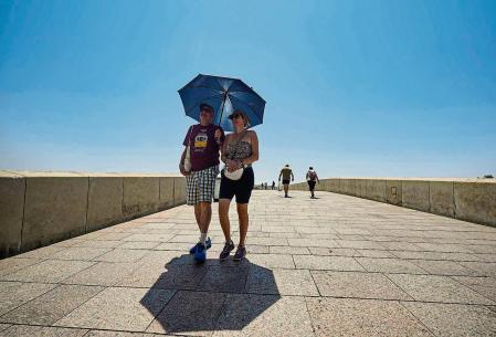 GRAFAND3105. CÓRDOBA, 26/06/2023.- Una pareja de turistas caminan bajo un paraguas para paliar los rayos de sol, este lunes por el Puente Romano de Córdoba, cuando la Agencia Estatal de Meteorología (AEMET) alerta de temperaturas significativamente altas, que pueden alcanzar los 44 grados en el valle del Guadalquivir por lo que se ha activado el aviso rojo en gran parte de Andalucía. EFE/Rafa Alcaide