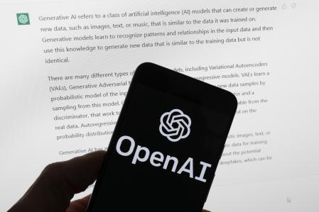 El logotipo de OpenAI en un teléfono móvil frente a una pantalla de computadora que muestra el resultado de ChatGPT.