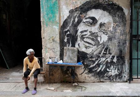 An elderly woman sells beans and cigarettes next to a mural depicting Jamaican singer Bob Marley in a street in Havana on January 30, 2024. (Photo by YAMIL LAGE / AFP)