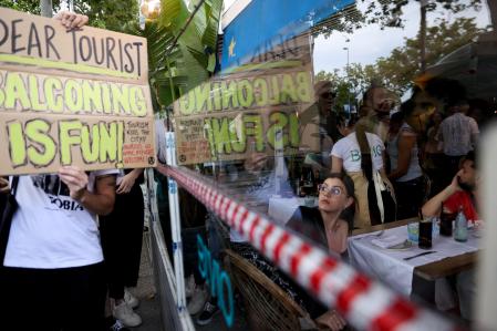 A tourist watches as demonstrators protest against mass tourism in Barcelona, Spain, July 6, 2024. The Catalan capital received more than 12 million tourists in 2023 and expects more in 2024. REUTERS/Bruna Casas