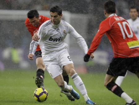 El jugador del Real Madrid, Cristiano Ronaldo, regatea ante los jugadores del Mallorca Josep Lluis Marti, y Julio Alvarez en el Santiago Bernabéu