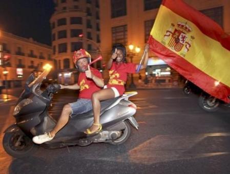 Una pareja convenientemente pertrechada con camisetas, bufandas, trompetas y banderas españolas celebra, en la plaza del Ayuntamiento de Valencia, el pase a la final de la selección española tras derrotar a Alemania