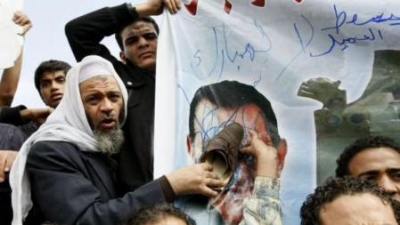 Varios manifestantes destruyen la imagen de Mubarak cerca de la plaza Tahrir en El Cairo