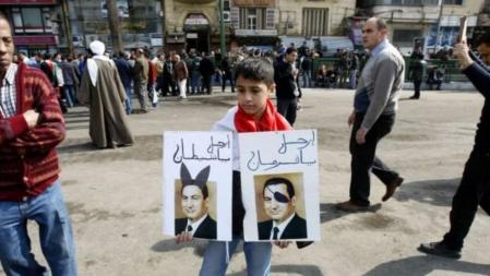 Un niño de seis años muestra la imagen de dos fotografías de Mubarak satirizado
