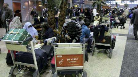 Unos turistas permanecen sentados en el aeropuerto de El Cairo mientras centenares de pasajeros esperan en la terminal información para abandonar el país