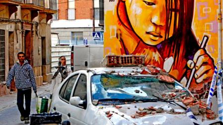 Una pareja camina cerca de un vehículo destruido por los escombros del terremoto registrado en Lorca