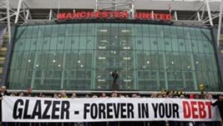 Imagen de una pancarta de aficionados del Manchester United frente a una de las entradas de Old Trafford y en la que acusan al propietario de sus deudas
