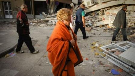 Una señora desolada por la tragedia se protege del frío con los escombros al fondo que reflejan la catástrofe en Lorca