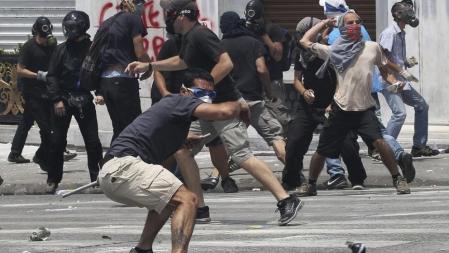 Los manifestanes llevan máscaras antigás mientras arrojan piedras hacia la policía antidisturbios, durante los enfrentamientos que se han sucedido en la segunda jornada de protestas dentro de la huelga general contra el nuevo plan de ajuste aprobado por el Parlamento