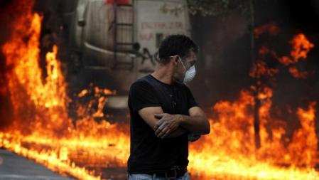 Un manifestante camina junto a un coche en llamas en Atenas durante las protestas contra las medidas de austeridad