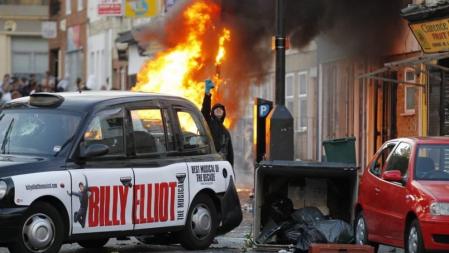 Un joven encapuchado desafía a la policia detrás de un taxi destrozado, durante los enfrentamientos vividos en el conflictivo barrio de Hackney, al este de Londres. Hackney fue hoy escenario de nuevos enfrentamientos entre la policía y un grupo de jóvenes que saquearon tiendas y atacaron autobuses. Según informó la cadena BBC, los disturbios se desencadenaron después de que la policía efectuara algunos registros en la calle, lo que dio lugar a que momentos después un grupo de encapuchados se enfrentara a los agentes arrojándoles piedras y botellas