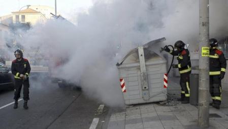 Los bomberos apagan el fuego de un contenedor de basura que había sido incendiado en el paseo de Canalejas de la capital salmantina, durante la jornada de huelga general