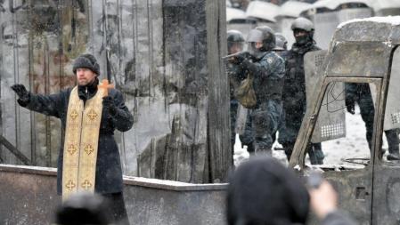 Un cura ortodoxo trata de calmar los ánimos de los manifestantes ante la dura vigilancia de los cuerpos de seguridad