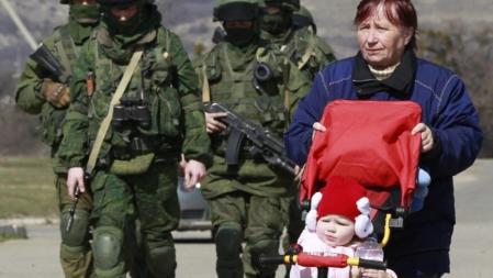 Una mujer pasea a su hijo junto a un grupo de soldados junto a un territorio militar ucraniano en la localidad de Perevalnoye a las afueras de Simferopol (Ucrania)