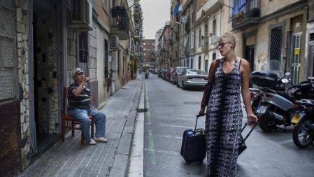 Una turista arrastra sus maletas por una calle de La Barceloneta, bajo la atenta mirada de un vecino