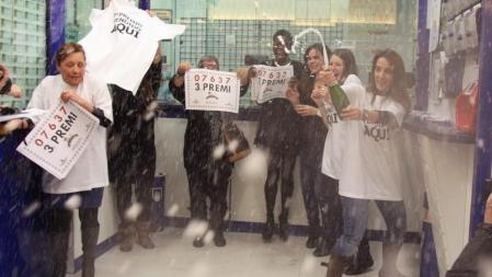 La lotera de la administración número 37 de L'Hospitalet (Barcelona) ubicada en un centro comercial (i), celebra junto a unos de los agraciados el haber vendido íntegramente el tercer premio de la Lotería de Navidad el 03637.