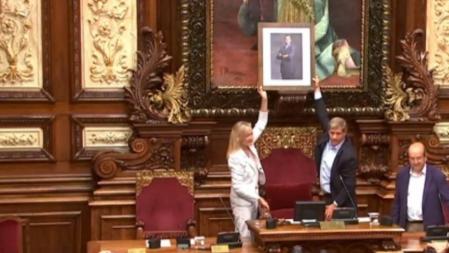 Alberto Fernández y Àngels Esteller sostienen la foto de Felipe VI en el salón de plenos del Ayuntamiento de Barcelona
